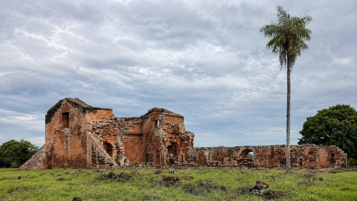 Ruins of the Jesuit mission of Trinidad in Paraguay with a green meadow and palm tree